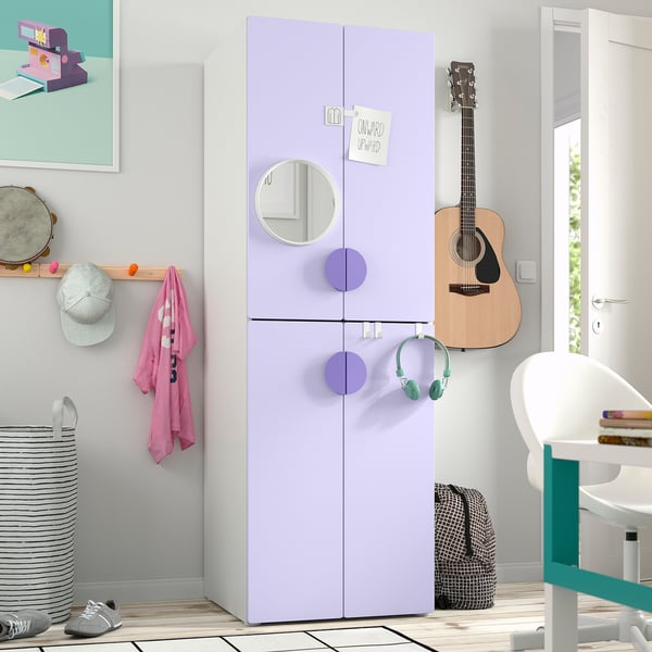 Un dormitorio infantil con un armario alto SMÅSTAD de color lavanda con puertas con espejos. Se encuentra entre una guitarra y un escritorio, más grande que los objetos cercanos.