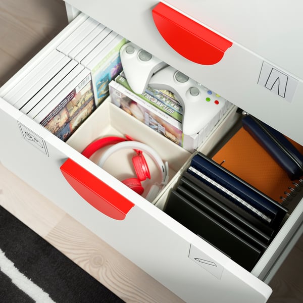 Cajones de almacenamiento abiertos con manijas rojas. Contiene mandos de juegos, libros y un cuaderno. Ideal para organizar los artículos de los niños.