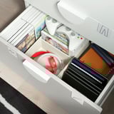 Un mueble de almacenaje SMÅSTAD blanco abierto con cajones y estantes abiertos, que contiene diversos artículos.