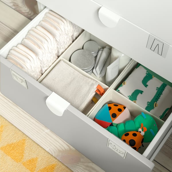Organizador de almacenamiento SMÅSTAD blanco con pañales, toallitas húmedas para bebés, mantas y juguetes coloridos en compartimentos.