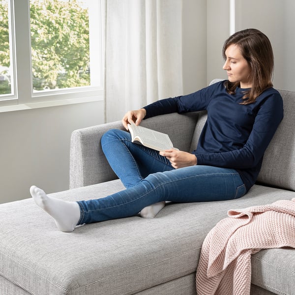 Persona leyendo en un sofá suave de patas altas junto a la ventana, cómodo, probablemente SMEDSTORP.