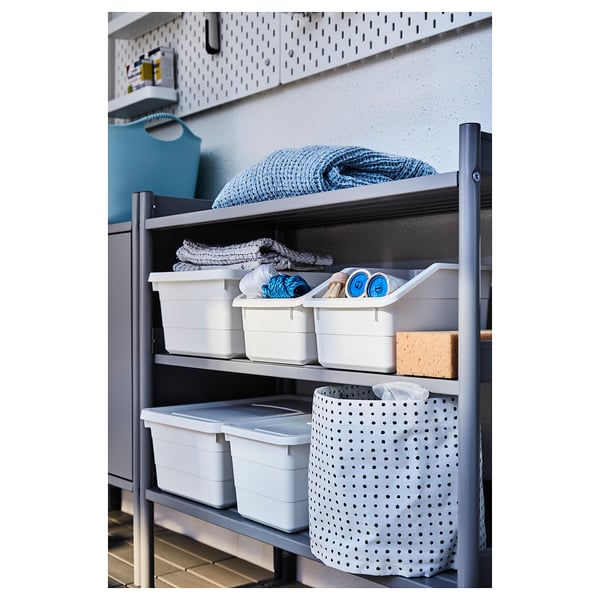 Una estantería de metal gris con contenedores de almacenamiento blancos y textiles doblados.