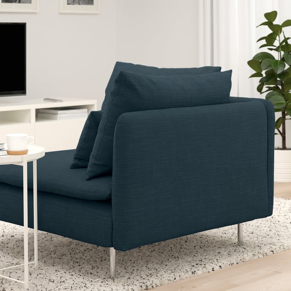 Sofá azul con cojines cuadrados sobre finas patas de metal en una acogedora sala de estar con mesa auxiliar y taza.