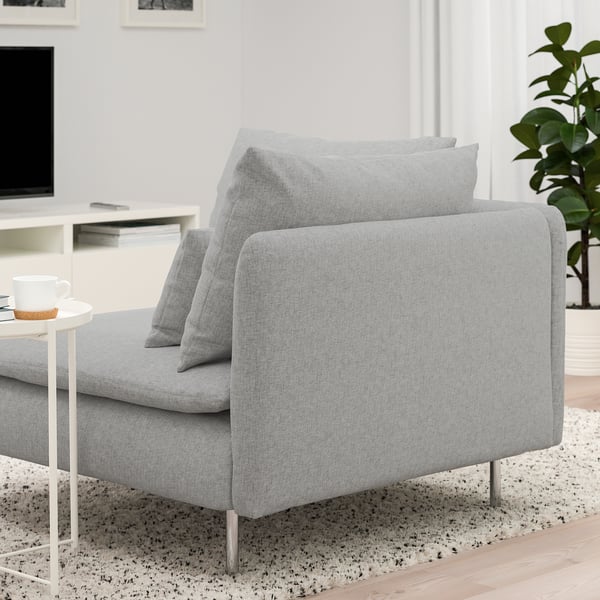 Un sofá moderno de color gris claro con cojines sobre una alfombra moteada. El sofá está diseñado con patas altas y asientos profundos para mayor comodidad.