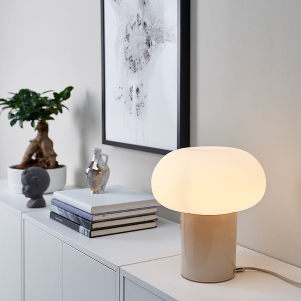 Sala de estar moderna con gabinete blanco. Lámpara de hongo beige, arte en blanco y negro, planta en maceta, pequeña escultura y libros apilados.