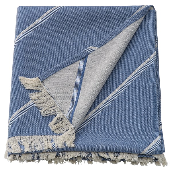 Una manta SOLUPPGÅNG azul doblada con flecos y bordes a rayas, con una mezcla de algodón y lyocell, diseñada para un uso acogedor.