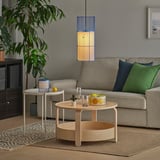 Sala de estar moderna con sofá beige, almohadas de colores y una lámpara colgante que proyecta luz decorativa. Una mesa de centro contiene fruta y un jarrón.