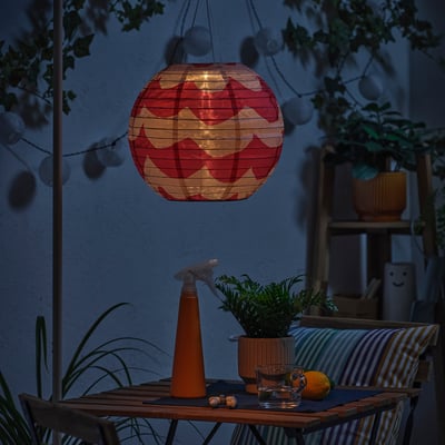 Patio oscuro con farolillo rojo. La mesa tiene planta, vasos, limón. Linterna incandescente.