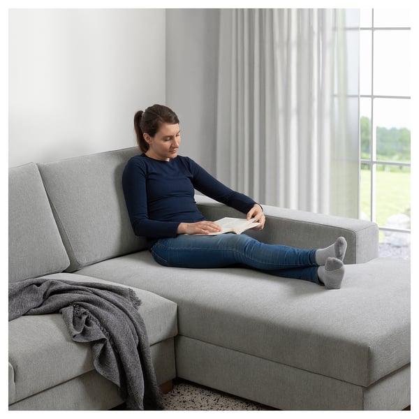 Mujer leyendo en un sofá seccional gris junto a la ventana.