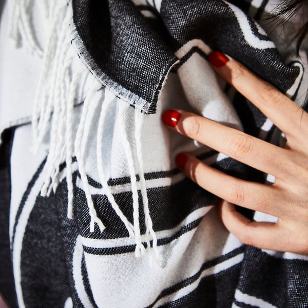 Mujer sosteniendo una elegante manta estampada en blanco y negro con extremos de flecos. Las uñas están pintadas de rojo.