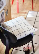 Silla negra con almohada de rejilla blanca, tarro de caramelos, suelo de madera, tablero de fotos.