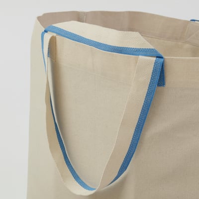 Bolso de algodón crema con ribete azul, asas grandes, logo pequeño. Duradero y lavable.