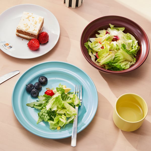 Tres platos coloridos: un plato turquesa con bayas y ensalada, un cuenco marrón con ensalada y un plato blanco con pastel y bayas.