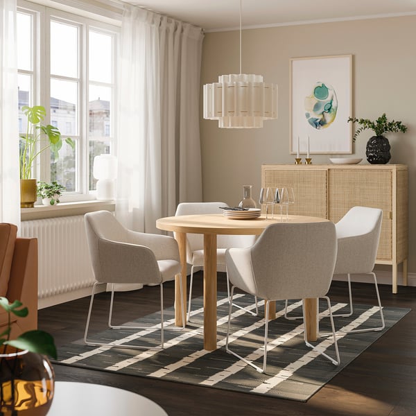 Comedor moderno con mesa de roble, sillas beige, lámpara colgante, alfombra gris y aparador con decoración.