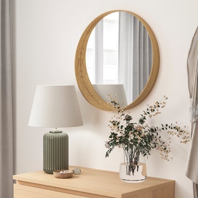 Decoración minimalista de la habitación: espejo redondo de madera, lámpara y jarrón blanco con flores secas sobre mesa de madera.