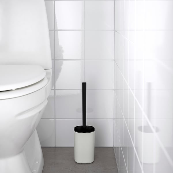 Escobilla de baño blanca en soporte negro junto a un inodoro en un baño minimalista.