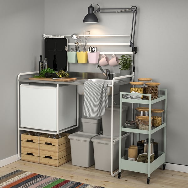 El pequeño carro de cocina blanco SUNNERSTA con cubos y estantes grises almacena los artículos de forma ordenada, ahorrando espacio en cocinas compactas.