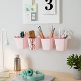 Escritorio con organizadores rosas que sostienen suministros de oficina, lámpara, auriculares, plantas y obras de arte.