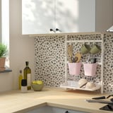 Cocina moderna con estante SUNNERSTA que sostiene recipientes rosas y tazas verdes, limones, aceite de oliva y condimentos cerca.