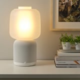 Moderna lámpara wifi y altavoz con luz cálida, plantas, libros e imágenes.