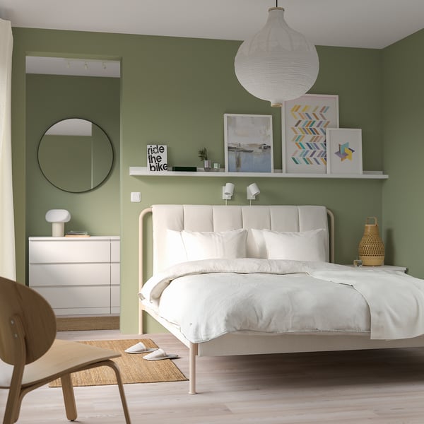 Dormitorio moderno con cama TÄLLÅSEN, cabecero acolchado, arte de pared verde, lámpara colgante, espejo, tocador y silla de madera.