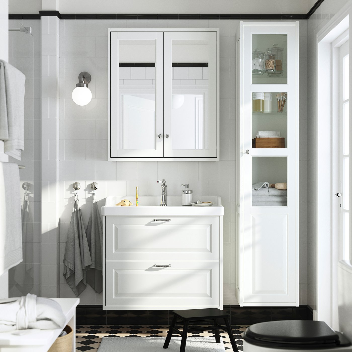 Baño moderno con tocador TÄNNFORSEN blanco, armario alto y suelo a cuadros. Lavabo, espejo y accesorios blancos.