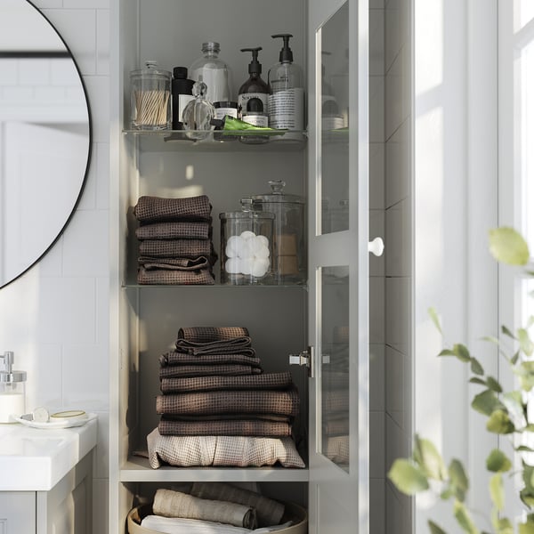 El armario de baño con puerta de vidrio organiza artículos de tocador, toallas, ropa de cama.