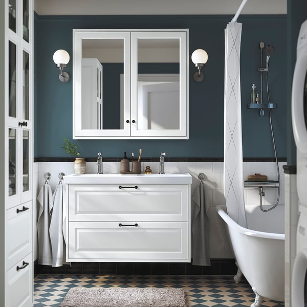 Baño blanco con pared azul, tocador de doble lavabo, piso a cuadros, tina de garra, ducha de vidrio.