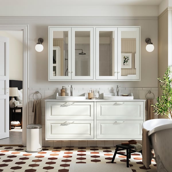 Baño moderno con doble tocador en color blanco. Dos lavabos, gabinetes con espejos y baldosas estampadas. Diseño limpio y minimalista.