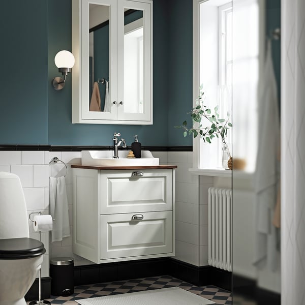 Tocador TÄNNFORSEN de pared, lavabo semiempotrado, suelo blanco y negro, radiador alto, paredes verde azulado, vegetación.