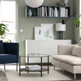 Sala de estar verde con mesa TIDTABELL, jarrones, alfombra beige, sofá blanco, silla azul marino y libros.