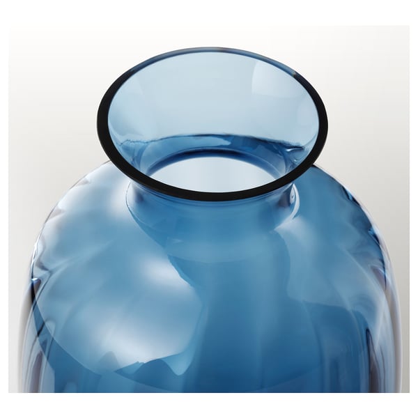 Jarrón de vidrio azul, hecho a mano con una parte superior de borde liso y redondeado, que refleja la luz en su superficie transparente.