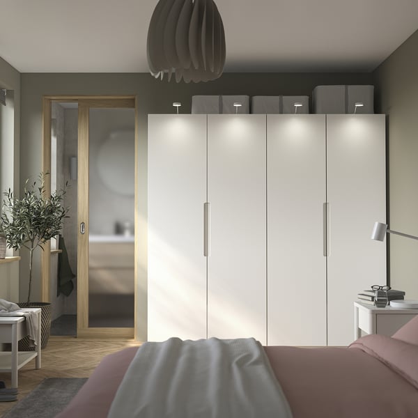 Dormitorio moderno con puerta de armario TONSTAD pax blanco, tiradores integrados. Incluye cama con manta gris y mesita auxiliar minimalista con lámpara.
