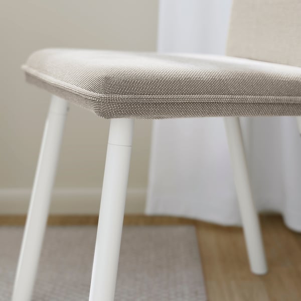 Silla con cojín beige, cuatro patas blancas, diseño moderno. Bordes suaves y redondeados, construcción robusta. Tapicería de calidad, asiento cómodo.