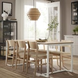Moderno espacio de comedor con mesa y sillas TRÄKUMLA, madera clara y blanco, tamaño para espacios pequeños, ventana abierta y estantes cercanos.