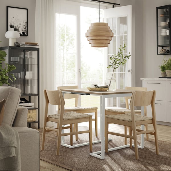 Comedor moderno con mesa TRÄKUMLA, madera clara, tamaño ajustable, sillas, lámpara, alfombra y gran ventanal.