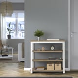 Salón moderno con consola TRÄKUMLA, pared gris, suelo de madera. Pequeña planta, libros, reloj y cajas en estantes. Puerta blanca al lado.
