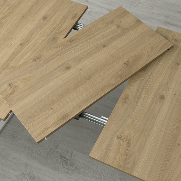 Muestra una mesa de madera con mecanismo de extensión ajustable, demostrando su capacidad de expandirse para obtener más espacio.