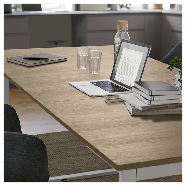 Moderna mesa de comedor de madera con sillas grises, ordenador portátil, tableta, libros y gafas.