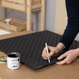 Aplicación de pintura TRIXIG sobre tablero perforado negro con pincel.