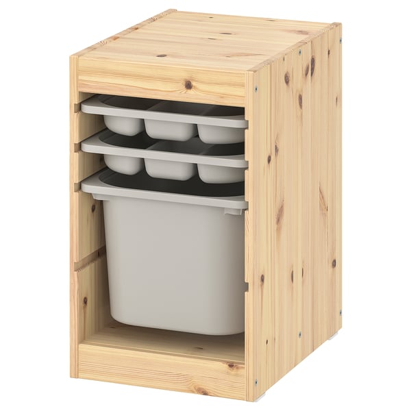 Un mueble de almacenamiento de madera IKEA TROFAST en pino claro, con tres bandejas de almacenamiento de plástico con compartimentos y un gran contenedor de plástico.