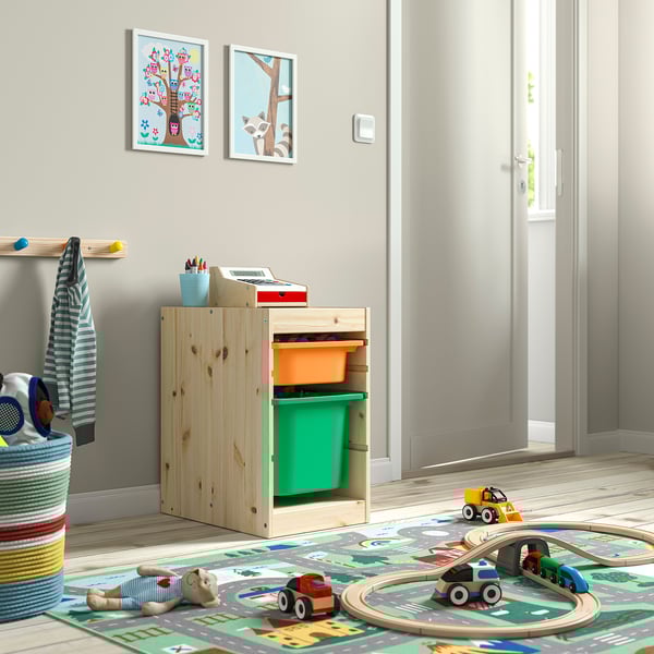 Área de juegos para niños con unidad de almacenamiento de madera TROFAST, contenedores de color verde brillante, juguetes y alfombras coloridas.