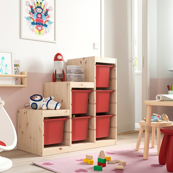Habitación para niños con almacenamiento de juguetes TROFAST, contenedores rojos, peluche de cohete y bloques sobre alfombra.