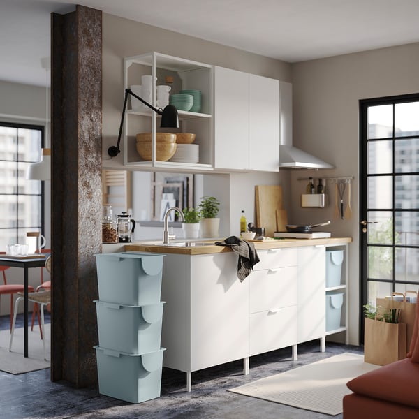 Cocina moderna con armarios blancos, gran ventanal y cubos TRÖSKNING azul claro bajo el fregadero.