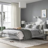 Cama moderna con tapicería gris, cabecero curvo y patas metálicas en amplio dormitorio.
