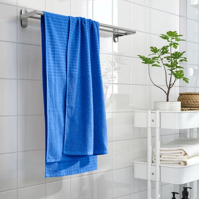 La toalla azul VÅGSJÖN cuelga en el baño, 100% algodón, gruesa y suave, junto al almacenamiento y la planta.