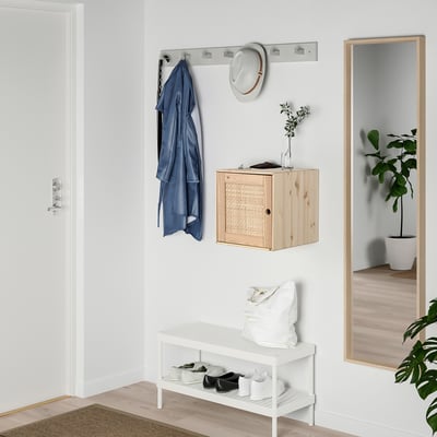 Pequeña configuración de entrada con gabinete VÄLJARE, con madera clara y textura tejida, abrigo azul colgante, sombrero blanco y plantas pequeñas.