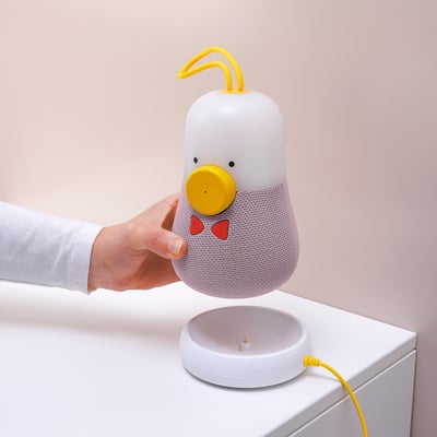 Una mano toca una lámpara de parlante de pato con detalles amarillos y rojos.