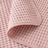 Colcha de algodón tejido suave de color rosa claro con superficie texturizada, que se muestra en primer plano y plegada.