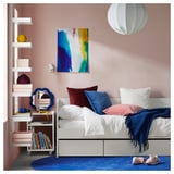 Dormitorio moderno con un sofá cama blanco, decoración azul y blanca, obras de arte coloridas y una estantería móvil.